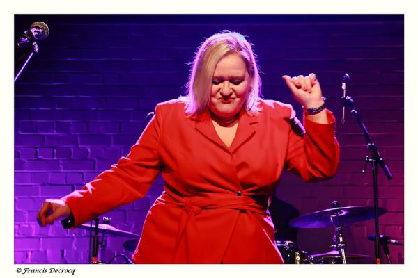 Emma Wilson appears in a pose on stage wearing a scarlet red outfit