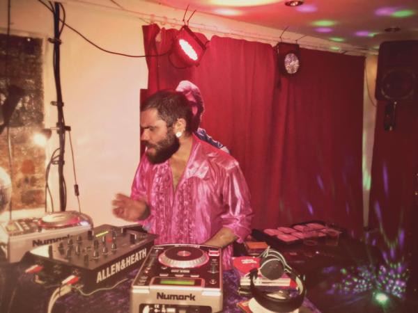 A fabulous bearded man DJ's wearing a silky pink shirt.