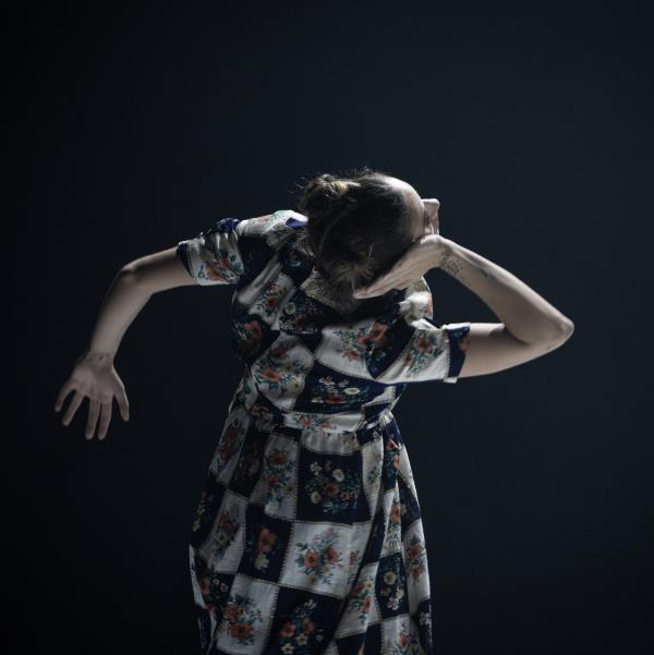 A woman dances with her hand to her ear in a graphic floral dress