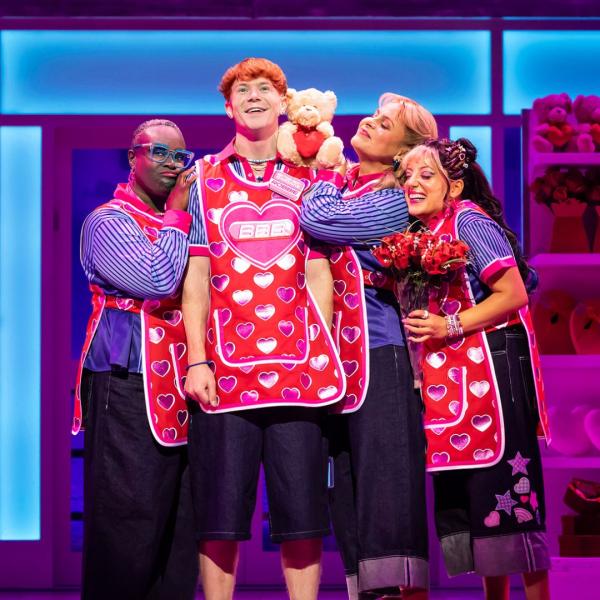 Four people wearing pink heart-patterned supermarket aprons embracing.