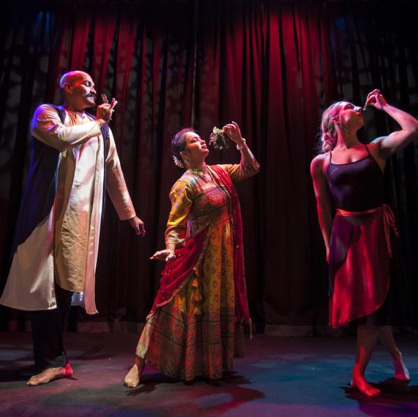 3 people stand on a stage in front of red curtain