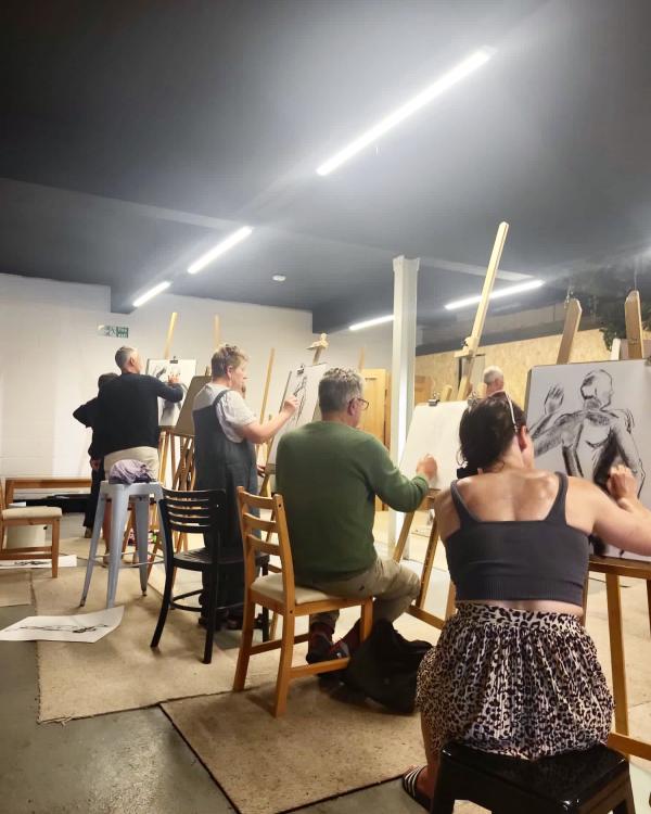 A group of of seated artists each at their own easel, drawing a life model