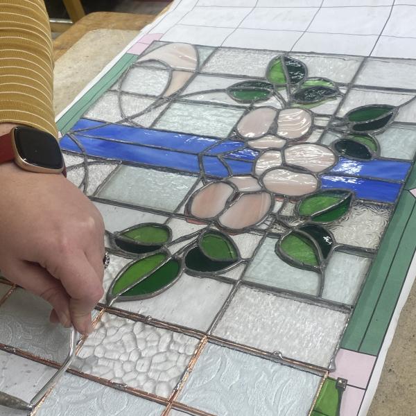 A hand adding solder to a stained glass piece of work