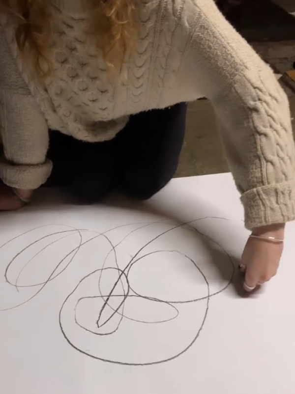 A workshop participant kneels on the floor drawing lines on a large piece of paper