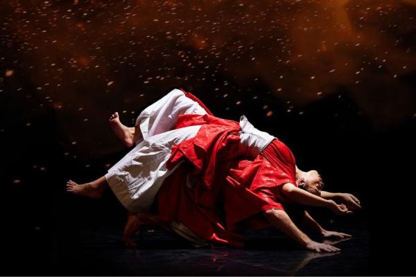 Two dancers in loose red and white clothing fall over each other