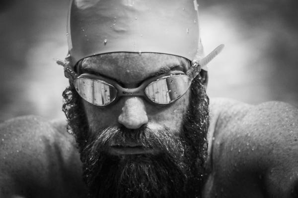 Black and white image of a man with a large beard in a pool with a swimming cap and goggles on.