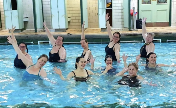 10 women in pool smiling and arms out stretched