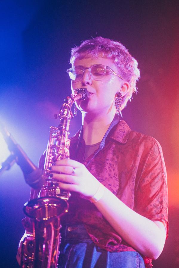 Flo Taylor playing an alto saxophone (center) lit up with blue (left) and red (right) stage lighting