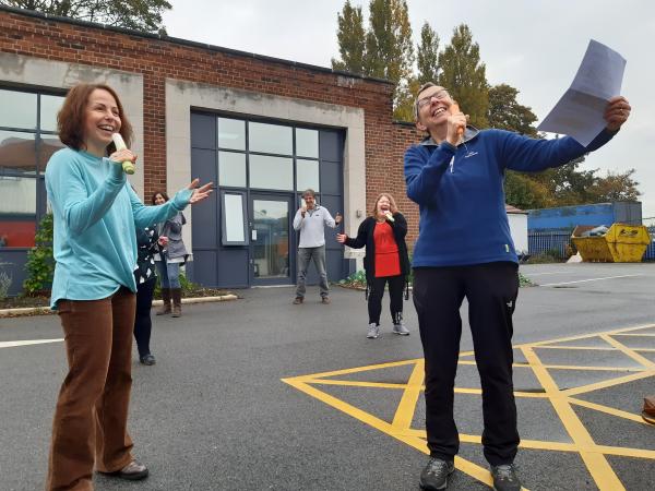 A group of people in a car park singing, using vegetables as microphones.