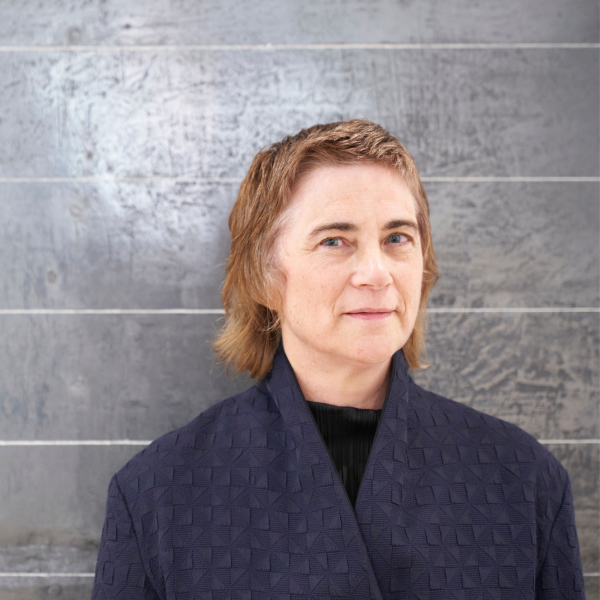 A white woman with short light brown hair wearing a blue blazer stood in front of a large graphite drawing with horizontal white lines