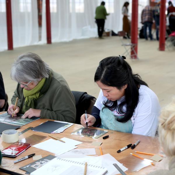 two workshop participants sit at a desk and work on their prints in an industrial mill space.