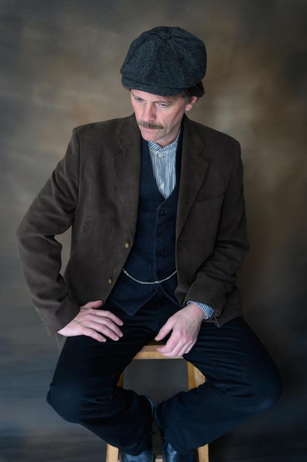 A man from the 1910's sits on a stool