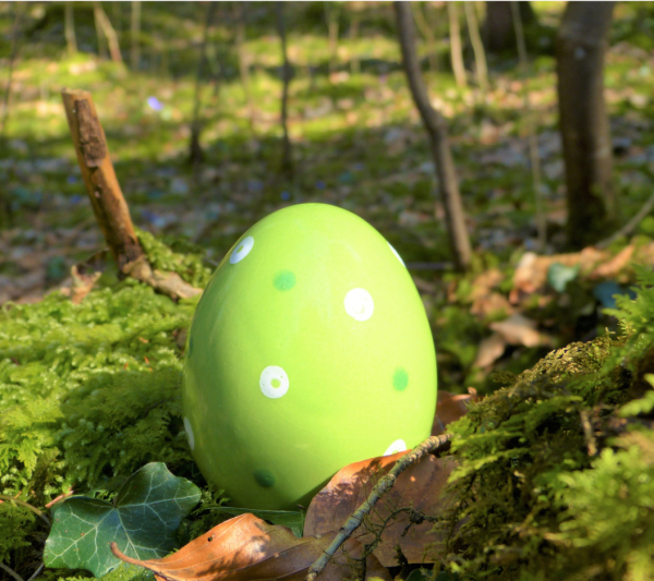 Photo of a green Easter egg on the ground in the woods.