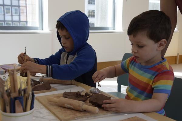 Two children sit side by side as they work on clay with various tools