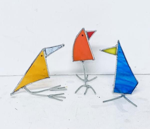 Three glass birds, one blue, one orange and one yellow stand up on silver coloured feet