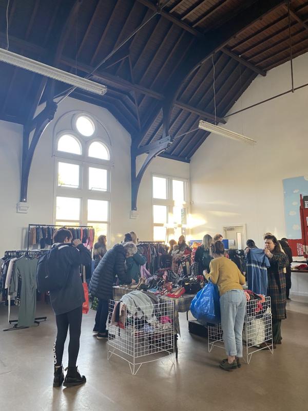 People rummaging in square containers filled with clothing. Rails of clothing can be seen in the background.