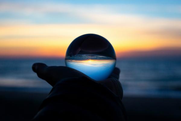 The image shows a hand holding a crystal ball reflecting the sunset.