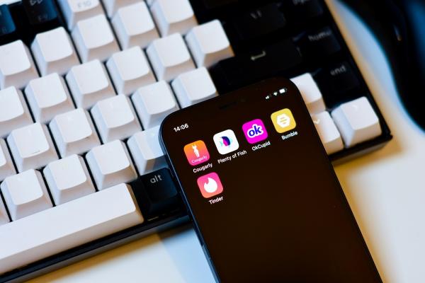 The image shows a smartphone displaying dating apps next to a computer keyboard.