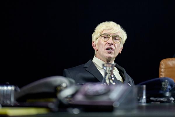 Steve Coogan wearing a suit and a blonde wig.