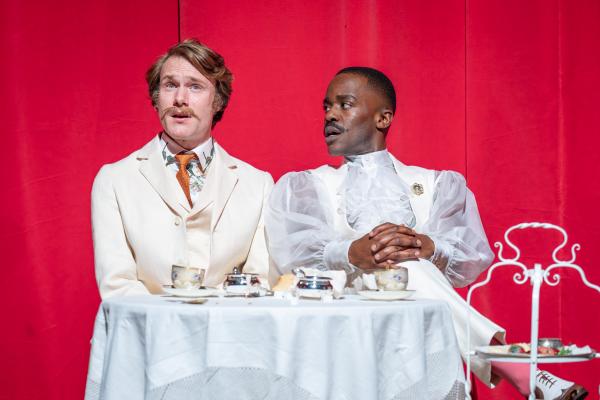 Two actors sat next to each other at a table both wearing white.