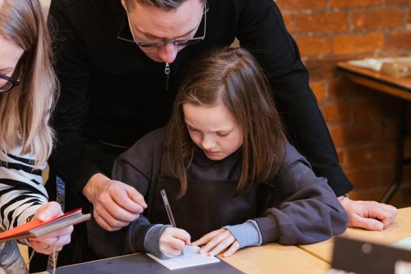 child sat a table drawing parent is assisting 