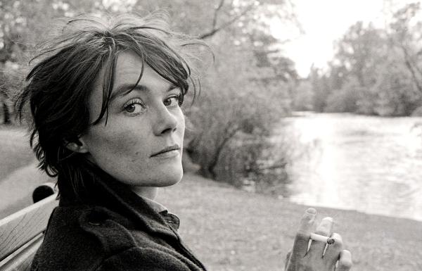 A black and white image of a woman sitting on a park bench, looking into the camera