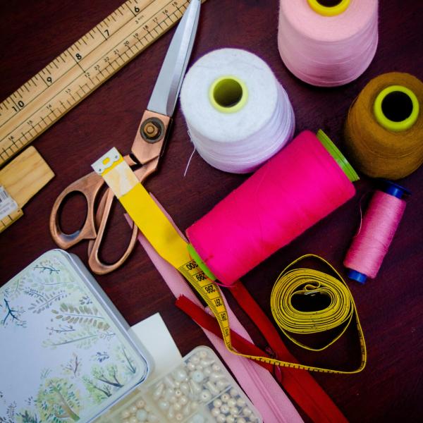 A flatlay of pink threads, golden scissors and a yellow tape measure