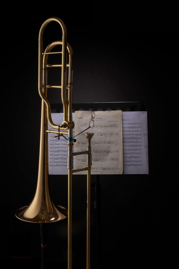 A trombone placed in front of a music stand with sheet music on it.