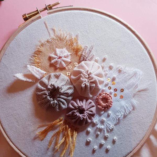 Embroidery hoop containing stitched flowers in muted tones. 