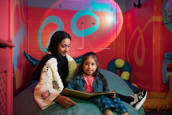 An image of a mother and daughter, smiling and reading in a colourful room.