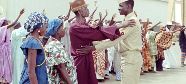 A line of black men and women in elegant clothing. Two men beginning an embrace