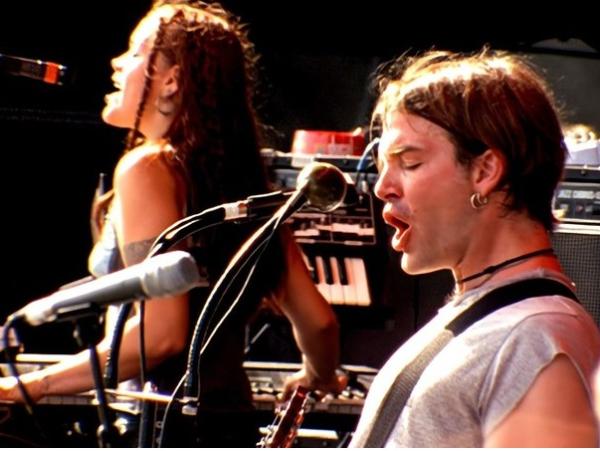 Woman with braids and a man with a earring play a rock concert