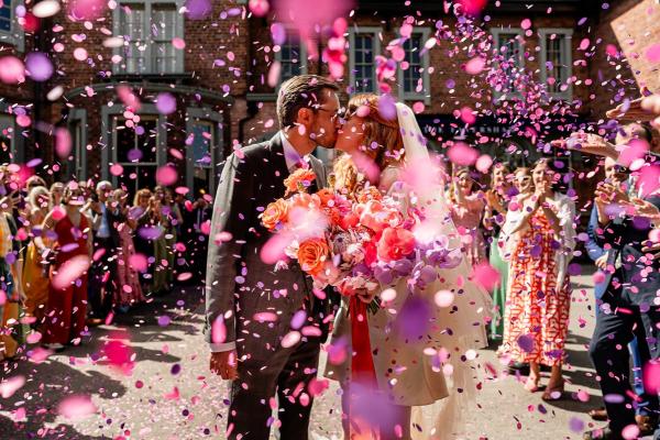 couple having a kiss whilst guests are throwing pink and purple confetti