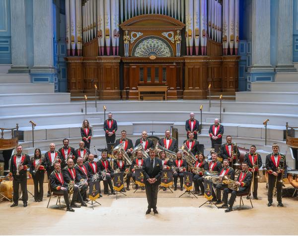 The members of Black Dyke Band in concert dress with their instruments sat in formation in Huddersfield Town Hall.