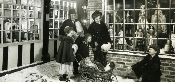 Black and white picture of a family dressed in period costume on Abbey House Museum Street, which has a festive feel with fake snow on the paved floor.