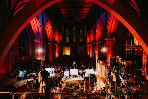 an orchestra performing in front of a crowd inside a church with the archways and band being lit up 