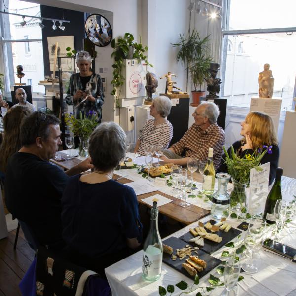 Woman demonstrating paper clay technique to people sitting around a wine tasting table in a sculpture gallery