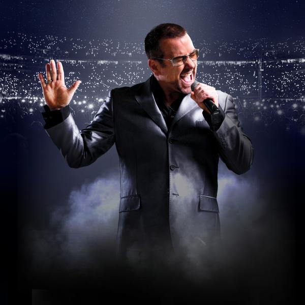 A George Michael tribute artist in a grey suit and sunglasses sings passionately into a microphone, in front of a packed crowd of torches. 