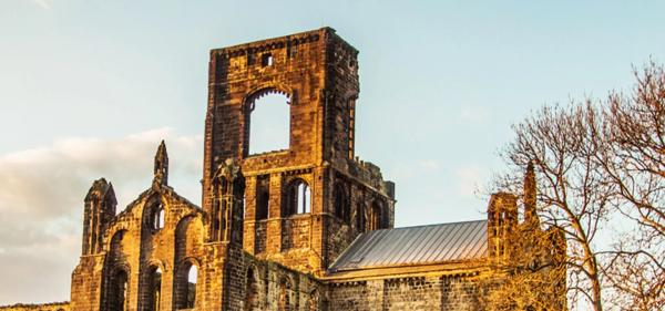 A picture of the Abbey in twilight, the collapsed tower of the nave visible.