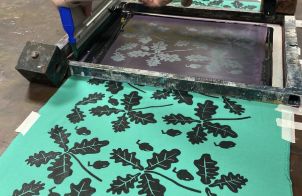 A pattern of leaves being screen printed in black on green fabric