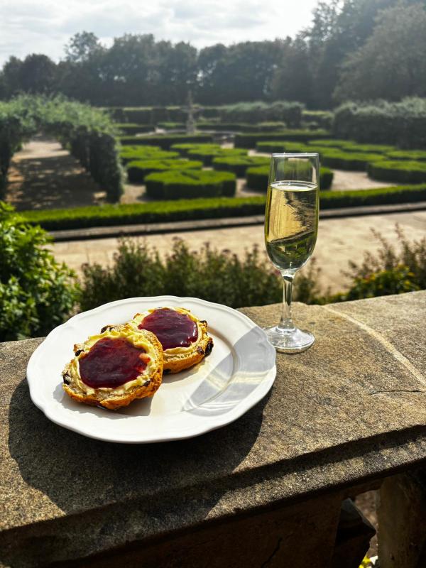 A plate of scones and a glass of champagne on a stone balcony, overlooking a garden