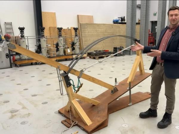 A photo of the Venn Bowling Machine, built from wood, with Thomas Glenday from University of Cambridge stood next to it