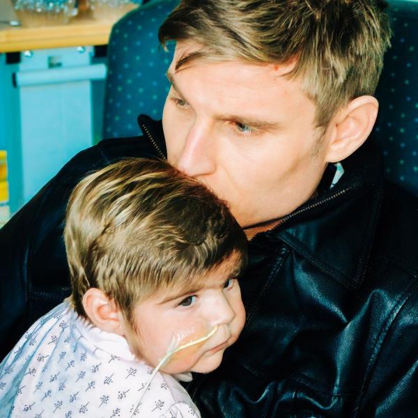 Digital photo of Scott Bennett comforting and holding a baby with an oxygen tube in his arms.