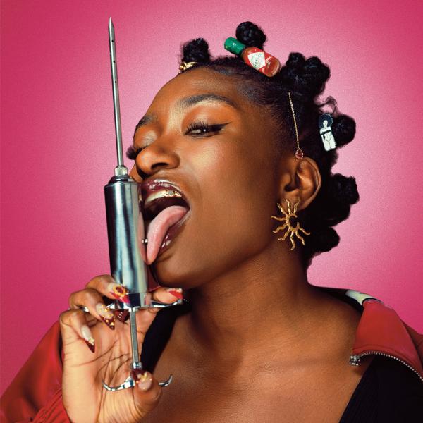 Sophie Duker sticking her tongue out and licking a metallic syringe, wearing fun jewellery and hairclips.