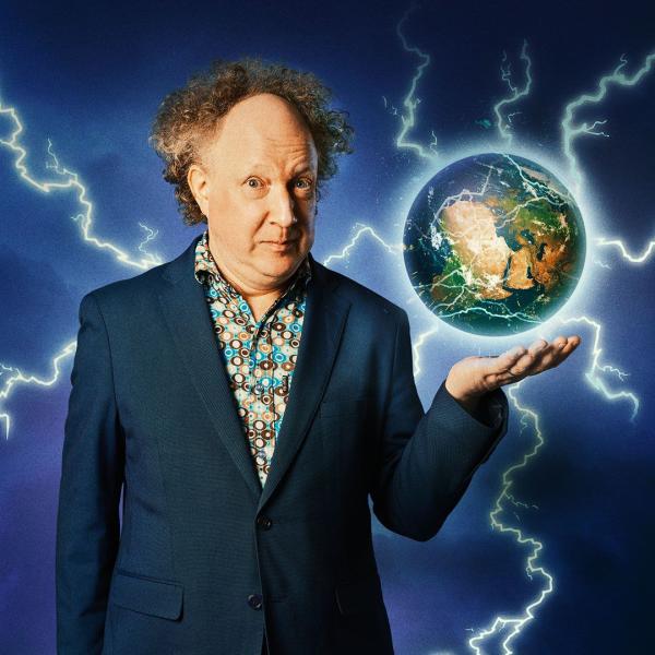 Andy Zaltzman stands in a suit jacket and patterned shirt. A globe emitting electricity and lightning bolts hovers above his outstretched hand.