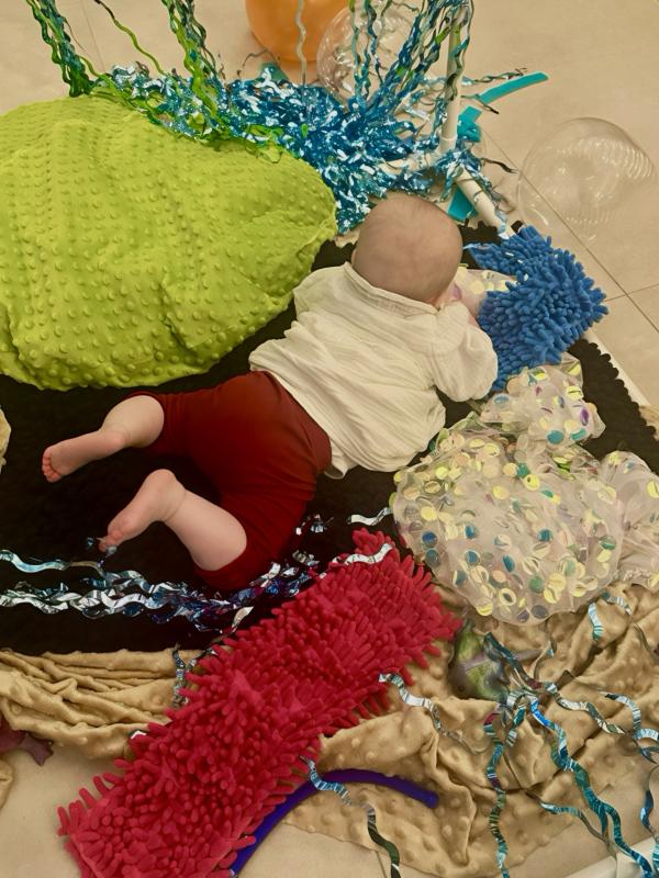 A baby on its belly playing with sensory items