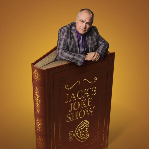 Wearing a chequered suit, Jack Dee emerges from a giant red book, the title reading 'Jack's Joke Show'.