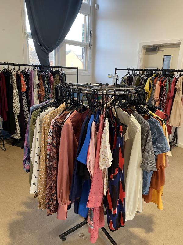 A circular rail filled wit colourful clothing. Long rails line the walls behind it.