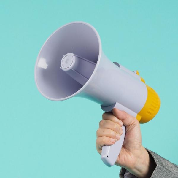 A photograph of a hand holding a grey megaphone against a blue background