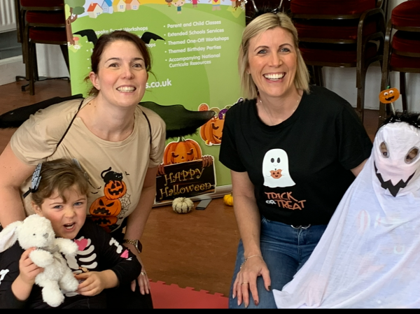 Two adult females sit behind two young children in halloween costumes. One Child is a skeleton and the other a ghost